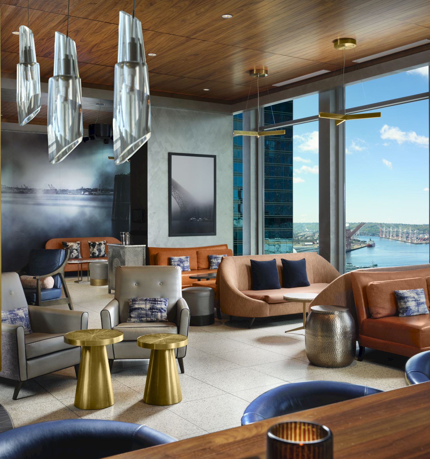 A modern lounge with stylish seating, unique lighting fixtures, and large windows providing a scenic view of a waterfront and Ferris wheel in the distance.